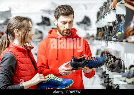 Mam und Frau in Rot Sport Kleidung wählen trail Schuhe für Wanderungen stehen in der Nähe des showacase des modernen Sports Shop Stockfoto