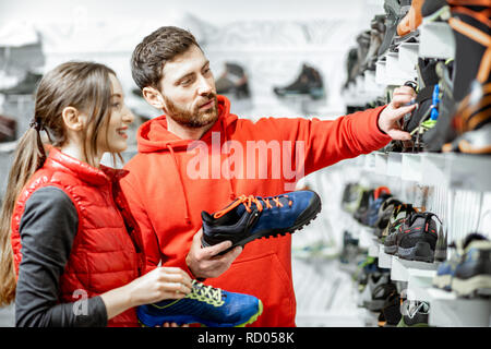 Mam und Frau in Rot Sport Kleidung wählen trail Schuhe für Wanderungen stehen in der Nähe des showacase des modernen Sports Shop Stockfoto