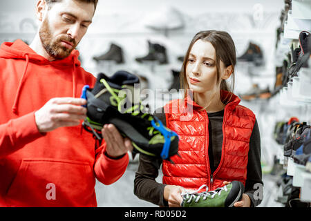 Mann und Frau auf die verzierten Schuhe für Wanderungen auf dem Eis stehen im modernen Sport Shop Stockfoto