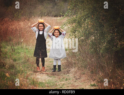 Zwei lächelnde Mädchen Kürbisse Holding auf ihre Köpfe, United States Stockfoto