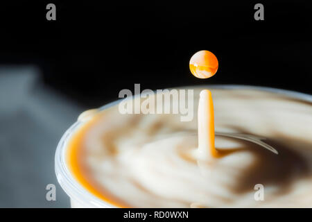 High speed Foto einer Karamell Milch Tropfen auf schwarzen Hintergrund im Studio Stockfoto