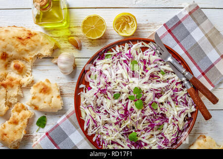 Ansicht von oben der klassischen Libanesischen Kohl Salat mit Zitronensaft, Olivenöl, Knoblauch, getrocknete und frische Minze in einem irdenen Schüssel auf eine Serviette mit Pita Stockfoto