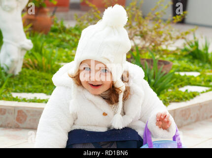 Hübsches Mädchen mit Wolle und Hut und weißen Mantel in einem Garten im Winter. Stockfoto