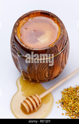 Duftende frische Honig fließt vom Fass und Honig Stick in einen Tropfen Honig mit einer Handvoll Pollen auf einem weißen Hintergrund. Close-up. Isoliert. Stockfoto