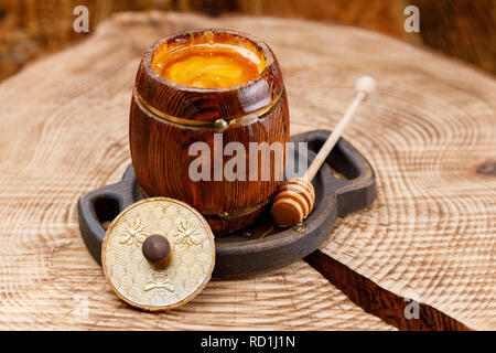 Fass mit einem duftenden flüssiger Honig und Honig stick Öffnen Sie auf einer hölzernen sah. Close-up. Stockfoto