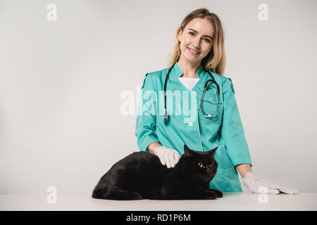 Lächelnd weibliche Tierarzt in der Nähe von Black Cat auf grauem Hintergrund Stockfoto