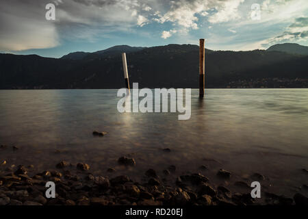 Holzpfählen im Wasser des Sees mit Alpen und bewölkter Himmel Stockfoto