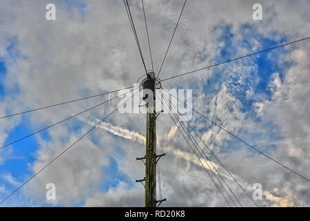 Traditionelle Telegraphenmast mit Anschlussdose und Kabel über eine teilweise bewölktem Himmel strahlt mit einem Flugzeug con Trail. Stockfoto
