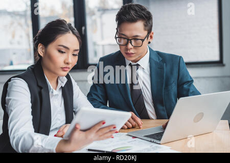 Junge asiatische Geschäftsleute arbeiten mit Laptop und einer Tablette im Büro ausgerichtet Stockfoto
