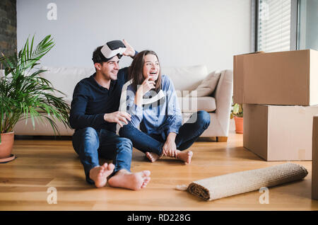 Ein junges Paar mit VR-Brille sitzen auf einer Etage, in einem neuen Haus zu bewegen. Stockfoto