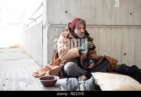 Die Vorderansicht des obdachlosen Bettler sitzen im Freien, holding Flasche Alkohol. Kopieren Sie Platz. Stockfoto