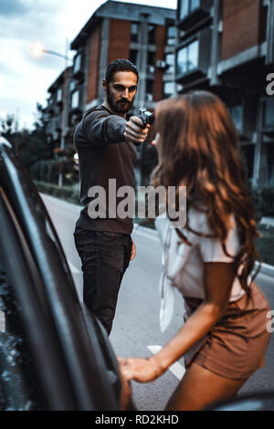 Bandit Raubüberfälle Frau mit Pistole und sie ist Gefühl schockiert und stehend mit dem Auto erschrocken. Stockfoto
