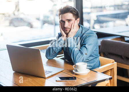 Wissen Sie nicht! Portrait von Traurigkeit gedrückt müde bärtige junge Freiberufler in Blue Jeans shirt sind allein sitzen im Café und auf der Suche nach einer Arbeit auf lapt Stockfoto