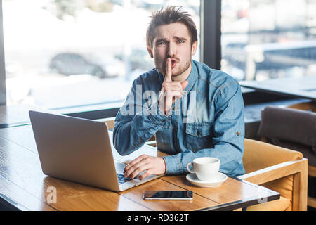 Werden Leise bitte! Portrait von Stattlichen schwere bärtige junge Freiberufler in Blue Jeans shirt Sitzen im Cafe und Arbeiten am Laptop, schlanke Finger auf Mo Stockfoto