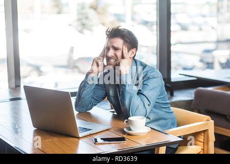 Warten, eine Idee! Seitenansicht Portrait von nachdenklich bärtige junge Freiberufler in Blue Jeans shirt Sitzen im Cafe und Arbeiten am Laptop, geschlossen Ey Stockfoto