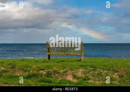 Eine Bank mit einem Regenbogen über der Nordsee Küste, im Benthall, Northumberland, England, UK gesehen Stockfoto