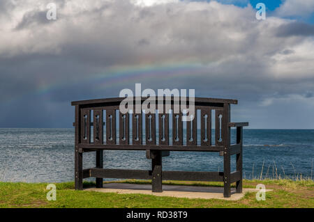 Eine Bank mit einem Regenbogen über der Nordsee Küste, im Benthall, Northumberland, England, UK gesehen Stockfoto