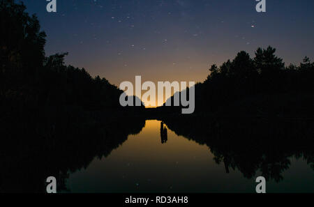 Helle Sonnenuntergang inmitten der dunklen Himmel über dem Fluss, im Wald. Sonnenuntergang an den Ufern des Flusses. Stockfoto