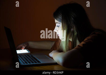 Ein hübsches junges Mädchen mit ihrem Laptop und Handy in der Nacht. Stockfoto