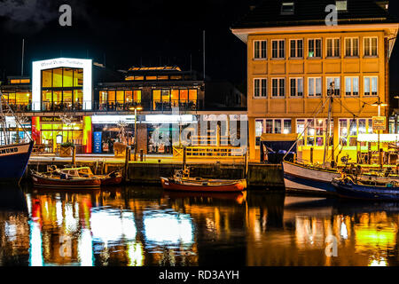 Beleuchtete Geschäfte und Cafés in der Abend, wie Boote Dock entlang der Alten Strom Kanal in die Ostsee Stadt Warnemünde, Deutschland. Stockfoto