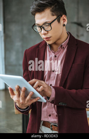Stattliche konzentrierte sich junge Unternehmer in Brillen mit digitalen Tablette im Büro Stockfoto