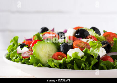 Griechischer Salat frisch in Schale mit schwarzen Oliven, Tomaten, FETA-Käse, Gurken und Zwiebeln auf weissem Holztisch. Nahaufnahme Stockfoto
