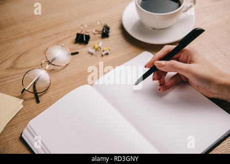 Teilweise mit Blick auf die Frau schreiben im Notebook am Arbeitsplatz mit Brillen und Tasse Kaffee Stockfoto