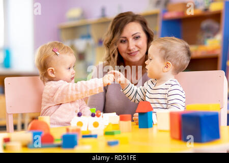 Kindergarten Lehrer auf der Suche nach Kinder im Kindergarten. Kleine Kinder Kleinkinder Mädchen und Jungen spielen zusammen mit Spielzeug. Stockfoto