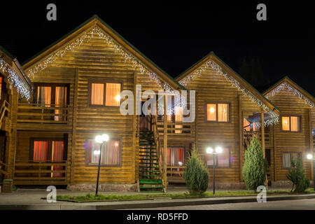 Zeile der neuen zweistöckigen ökologischen Holzmöbeln gemütlich eingerichteten Cottages Hotels auf sauberen beleuchtete Straße unter dunklen Nachthimmel. Tourismus und Recreatio Stockfoto