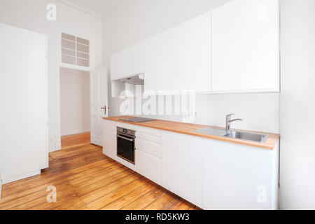 Leere, neue, integrierte Küche mit whote Möbeln und Holzboden - Stockfoto