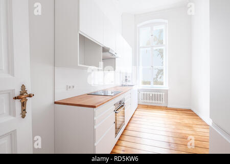 Leere, neue, integrierte Küche mit weißen Möbeln und Holzboden - Stockfoto
