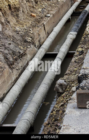 Wasserleitungen, isolierte Dachbahnen während der Reparatur in einem Graben gefüllt mit schlammigen Flüssigkeit. Stockfoto