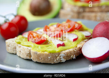 In der Nähe von Toast mit Avocado, Tomaten und Radieschen und die Zutaten auf einer Platte Stockfoto