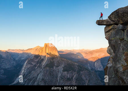 Eine furchtlose Wanderer steht auf einem überhängenden Felsen genießen den Blick auf die berühmten Half Dome am Glacier Point in schönen Abend dämmerung Blicken Stockfoto