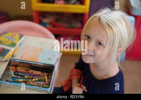 Eine 5 Jahre alte Blonde kaukasische Mädchen griffen einen Zeichenstift während der Färbung, und lächelt in die Kamera. USA. Stockfoto