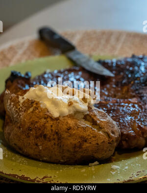 Eine gebratene Ribeye, oder Rib Eye Steak gekocht Medium gut mit einer gebackenen Kartoffel und saure Sahne auf einem Teller zu tun. USA. Stockfoto
