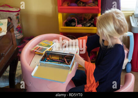 Eine fünf Jahre alte Blonde kaukasische Mädchen Arbeiten am Schreibtisch eines Kindes mit Buntstiften, zeichnen ein Bild. USA. Stockfoto