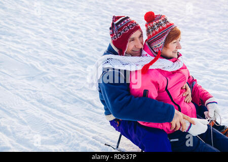 Senior paar Schlitten bergab. Familie Spaß haben, sitzen auf dem Schlitten im Winter Park. Valentinstag Konzept Stockfoto
