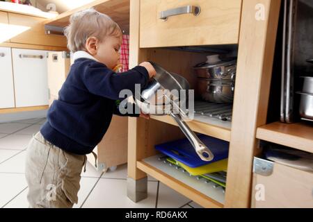 Junge, 10 Monate, wobei Kochtöpfe aus einem Schrank in der Küche Stockfoto