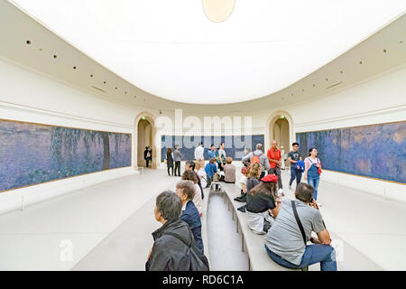 Menschen, die die Seerosen von Claude Monet in geschwungenen Tafeln in einem ovalen Raum in der Orangerie oder im Musée de l'Orangerie in Paris, Frankreich, betrachten Stockfoto