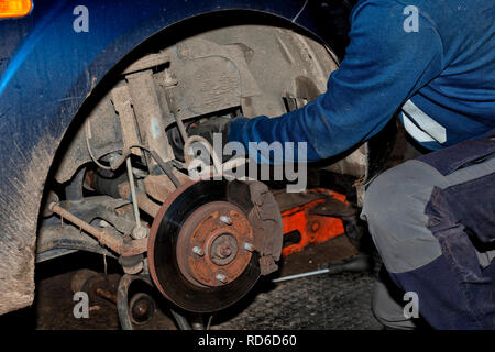 Ein Mechaniker arbeitet auf seinem Knie auf dem Boden der Instandsetzung einer alten Auto. Stockfoto