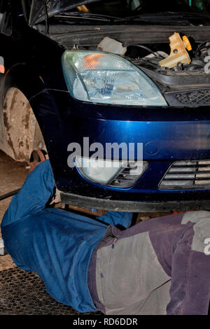 Ein Mechaniker arbeitet auf dem Boden liegend Instandsetzung einer alten Auto. Stockfoto