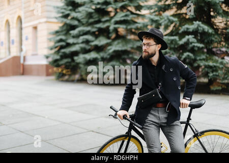 Gut aussehender bärtiger Mann im stilvollen Outfit auf der Straße mit einem Fix Gear Fahrrad Stockfoto