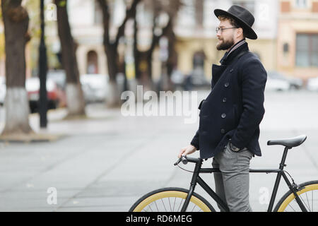 Gut aussehender bärtiger Mann in Gläsern und Kappe mit Fahrrad und lächelnd Stockfoto