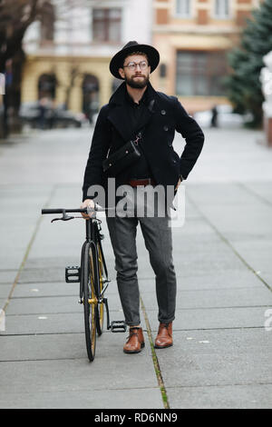 Gut aussehender bärtiger Mann im stilvollen Outfit auf der Straße mit einem Fix Gear Fahrrad Stockfoto