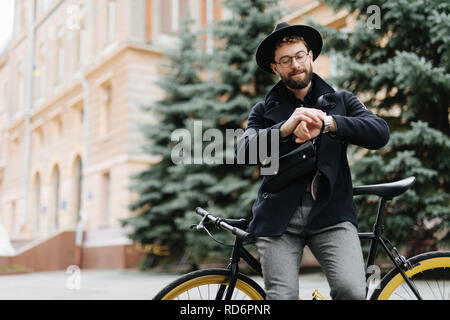 Gut aussehender bärtiger Mann, der einen Bruch sitzt auf einem Fahrrad auf die Uhr schauen. Stockfoto