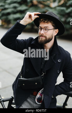Gut aussehender bärtiger Mann im stilvollen Outfit auf der Straße mit einem Fix Gear Fahrrad Stockfoto