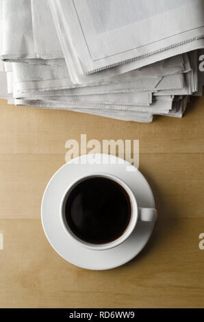 Overhead shot eine Tasse schwarzen Kaffee mit Untertasse auf hellem Holz Laminat Tisch mit Stapel von Zeitungen. Stockfoto