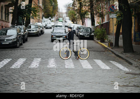 Mann mit einem fixie Fahrrad zu Fuß auf der Straße. Junge Hipster mit retro Fahrrad Wandern auf dem Zebrastreifen. Stockfoto