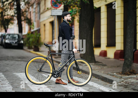 Menschen, Stil, Stadt leben und Lifestyle. Junge hipster Mann mit Schulter- und fixed Gear bike Crossing crosswalk auf der Straße Stockfoto